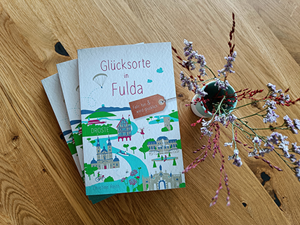 Drei Ausgaben des Glückortebuchs auf einem Holztisch mit Trockenblumen dekoriert