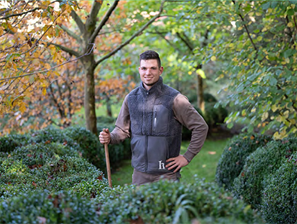 Ein junger Gärtner in Arbeitskleidung in einem Garten zwischen Buchsbäumen